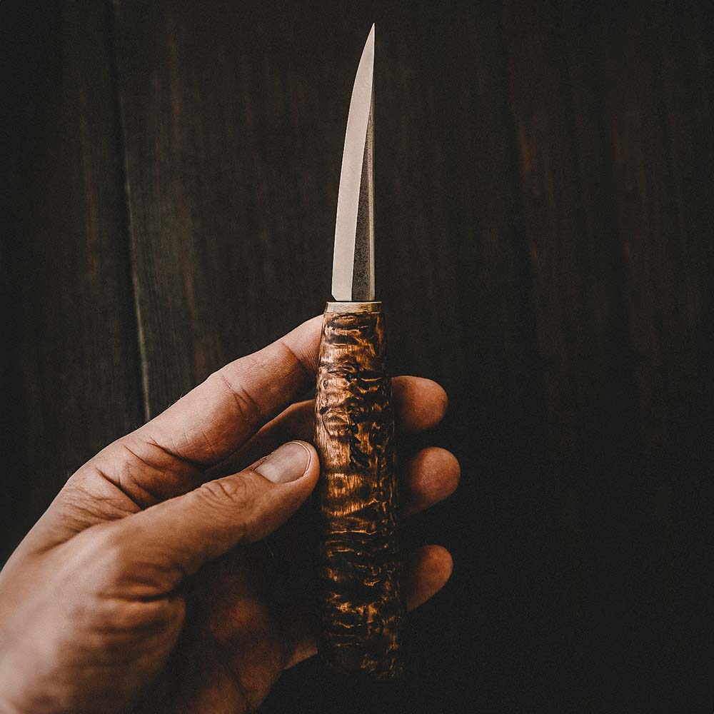 Roselli's handmade Finnish Carving knife with a handle made from stained curly birch and a blade from carbon steel with a scandi grind zero feature. Comes with a handmade leather sheath.