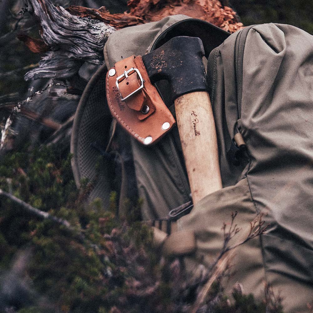 Handmade Finnish outdoor axe from Roselli laying in a backpack. Made with a short handle comes with a axe case in light vegetable leather